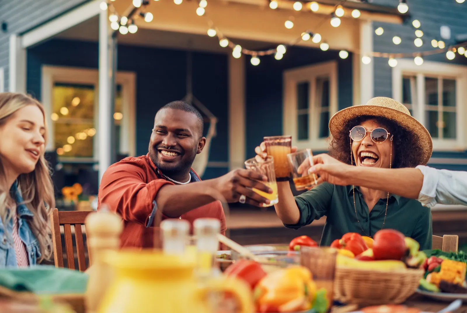 Friends sharing food and raising glasses around an outdoor table in warm Spring light