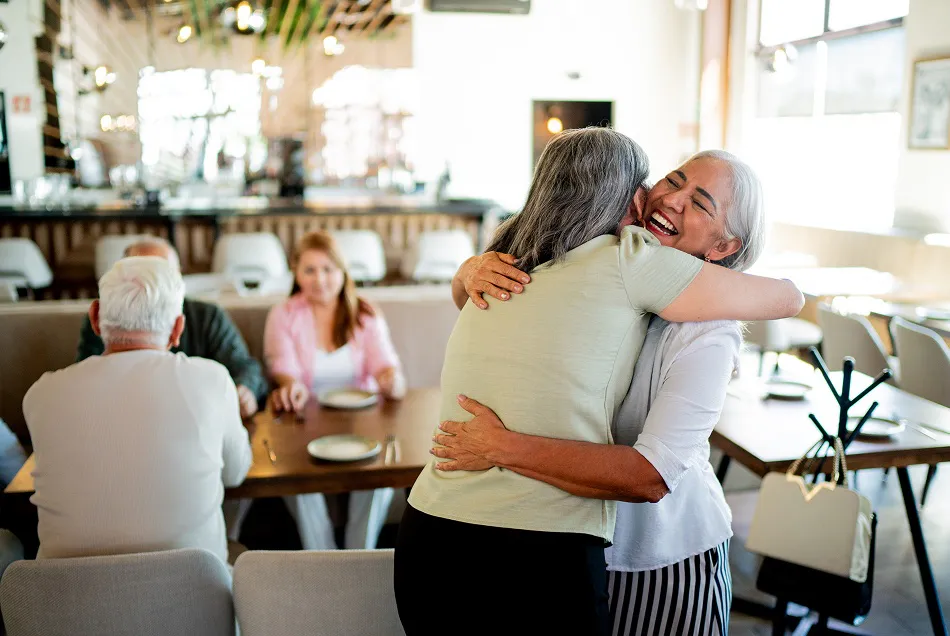 Two friends greeting each other warmly at a bright restaurant
