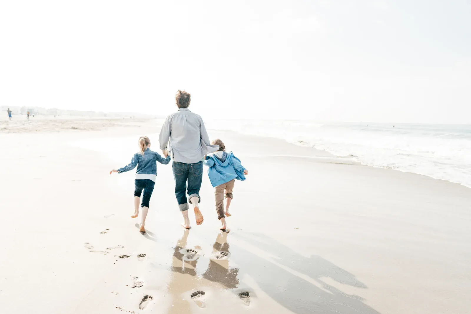 A father walking along a bright beach with two children